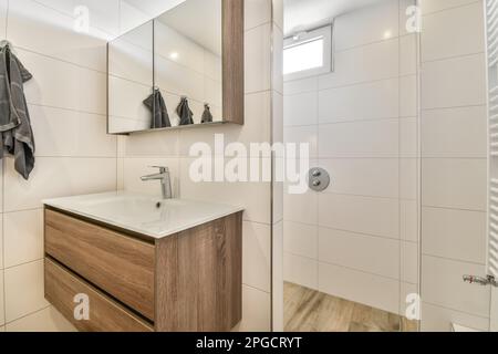 Interior design of modern shower bathroom with white tiled walls and window on top with sun reflecting glass while mirror cabinet placed above sink wi Stock Photo