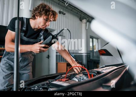 Tests car's electronics. Adult man in grey colored uniform works in the automobile salon Stock Photo