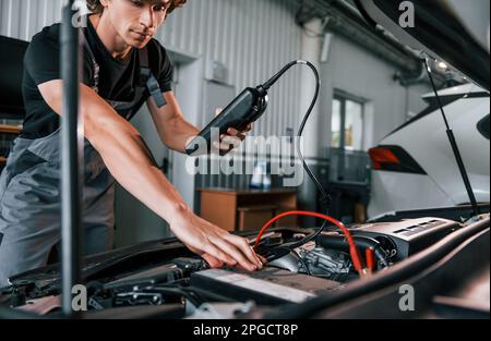 Tests car's electronics. Adult man in grey colored uniform works in the automobile salon Stock Photo