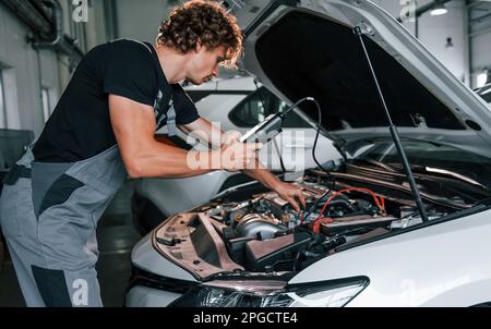 Tests car's electronics. Adult man in grey colored uniform works in the automobile salon Stock Photo