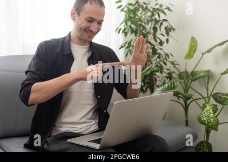 Young man showing gesture in sign language using laptop, make video call Stock Photo