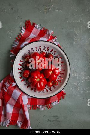 Top view of fresh red cherry and beef tomatoes placed on plate over checkered cloth on gray table background Stock Photo