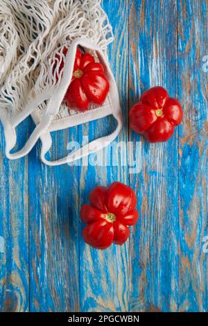 Top view of fresh ripe red tomatoes with eco friendly cotton mesh bag placed on blue stripped wooden table Stock Photo