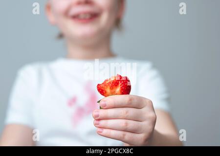 A child's hand is holding a slice of strawberry. A dirty red stain on the front of a white t-shirt Stock Photo