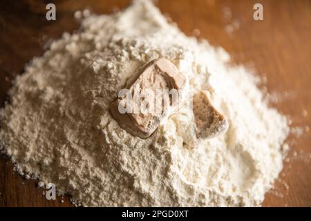 A cube of  yeast crumbled on the flour Stock Photo