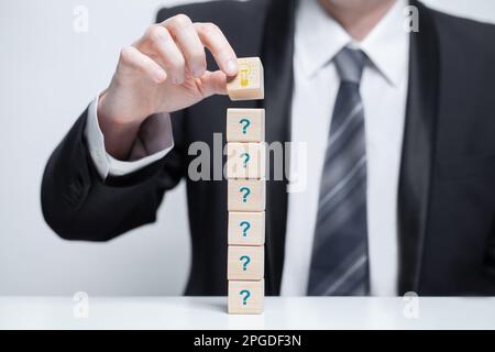Questions marks on wooden block pyramid in businessman hand. FAQ question concept Stock Photo
