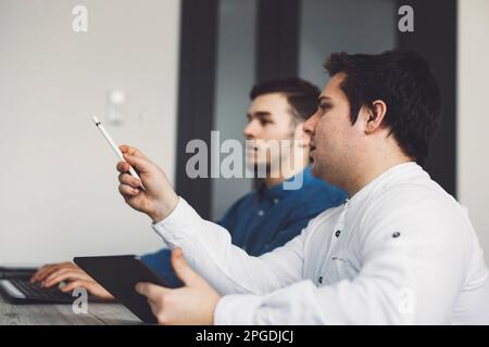 Side view, waist up two caucasian male programmers sitting by the office desk discussing something Stock Photo