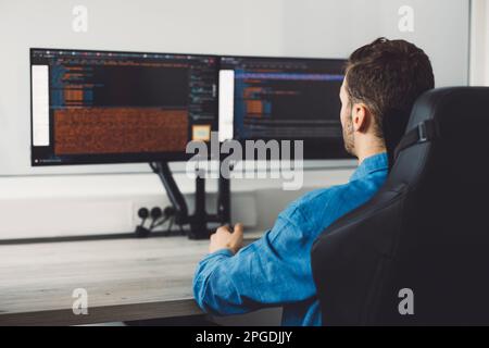 Over the shoulder view of IT programmer working on two screens in the office  Stock Photo