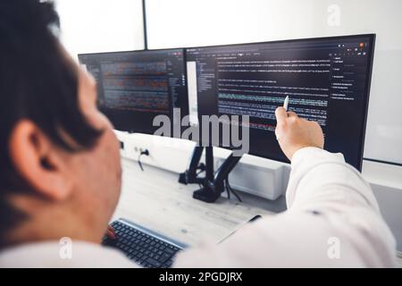 Close up over the shoulder view unrecognizable man, programmer coding, pointing at something on the computer screen  Stock Photo