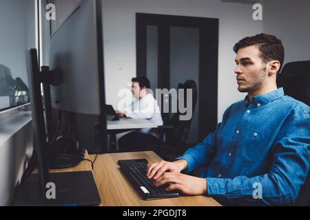 Side view, two programmers working in the office coding on desk top computers  Stock Photo