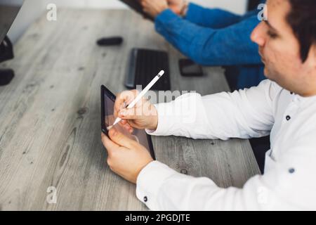 Close up IT specialist writing on a digital tablet, sitting by the office desk next to a colleague  Stock Photo