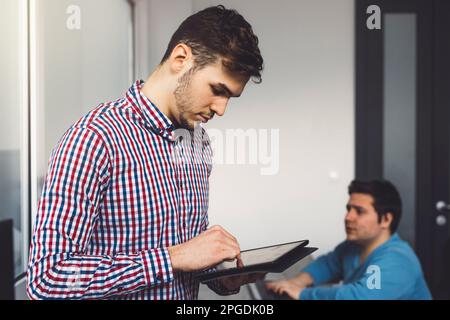 Waist up IT guy wearing a blue and red shirt working on a digital tablet in the office  Stock Photo