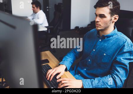 Young man in a blue shirt a programmer typing on keyboard while looking at the computer screen, coding  Stock Photo
