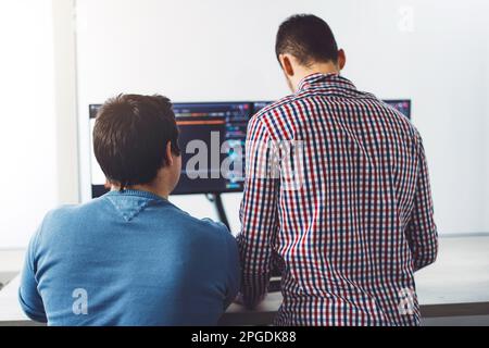Back view of two young IT guys in front of computer screens, writing a new code  Stock Photo