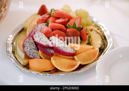 Fruit salad with strawberries, oranges and pitaya in a plate on a white tablecloth, close-up Stock Photo