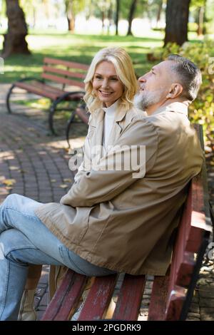 Positive blonde woman sitting near mature husband on bench in park,stock image Stock Photo