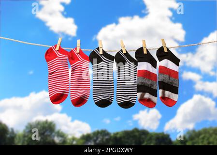 Clean washed striped socks hanging on clothesline to dry outdoors on sunny summer day. Clothesline with red, gray and white socks against blue sky Stock Photo