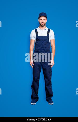 Full size fullbody portrait of attractive cheerful deliver in blue uniform with stubble looking at camera holding, isolated on grey background Stock Photo