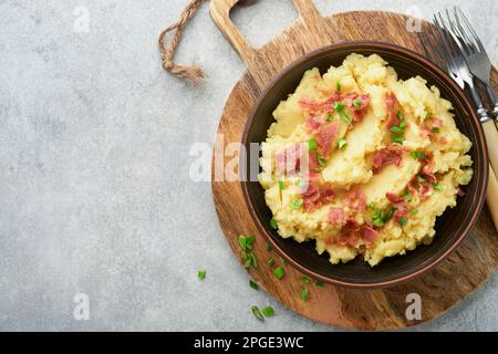 Mashed boiled potatoes. Bacon mashed potatoes with green onion, pepper and cheddar cheese in bowl on light old wooden backgrounds. Delicious creamy ma Stock Photo