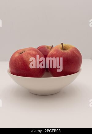 Three small red apples in a white cup. Vertical and close-up. Stock Photo