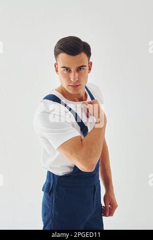 Shows biceps. Ready to work. Male worker in blue uniform standing inside of studio against white background Stock Photo