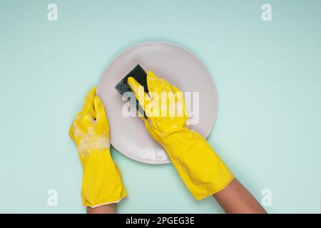 woman in yellow cleaning gloves on light color background cleaning plate with cleaning sponge Stock Photo
