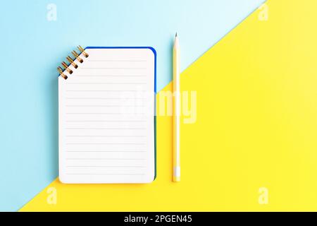 Open notebook with empty page and yellow pencil on two color blue and yellow background with blank space. Top view, business, education concept. Stock Photo