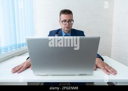 Young employee wearing glasses looking at computer monitor during working day in office. focused reading of information on a laptop in the office. The Stock Photo