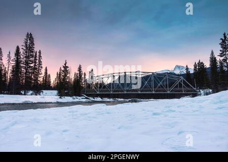 Beautiful sunrise over snowy rocky muntains and the bridge cross the river in pine forest on winter at Banff national park, Alberta, Canada Stock Photo