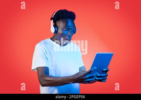 Amazed black man with headphones and tablet on red Stock Photo