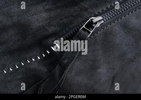 Zip with a tab on a black suede jacket with white contrasting seams background close up Stock Photo