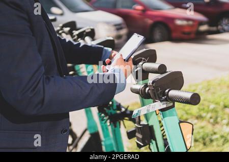Electric scooter in city. Man using smartphone to rent an e kick vehicle. guy with mobile phone using eco transportn. Business person in traffic. Mode Stock Photo