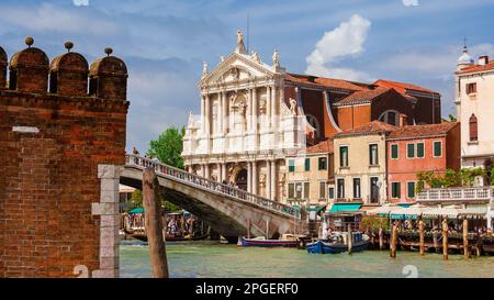 Sightseeing in Venice. Tourists cross Scalzi Bridge on Grand Canal next to the railway station, with beautiful St Mary of Nazareth Church Stock Photo