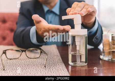 A businessman cleans his hands of bacteria and germs using a table sanitizer in a restaurant before lunch. Disinfection from coronavirus. Stock Photo