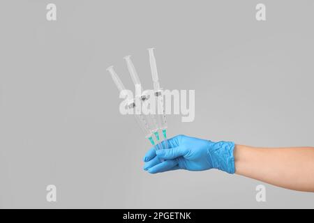 A hand in a blue glove holds three syringes with a coronovirus vaccine. Syringes with medicine in the doctor's hand on a gray background. Vaccinations Stock Photo