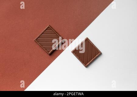 Two chocolate bars on colored backgrounds top view. Small chocolate bars on white and brown backgrounds. Conceptual composition of two chocolate bars Stock Photo