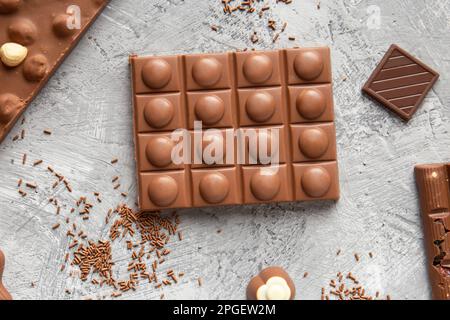 Milk chocolate bars of different sizes, sweets, chocolate chips on a gray background top view. Handmade chocolate with hazelnuts close-up. Stock Photo