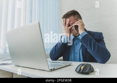 Tired or exhausted man closing his face with hands sitting in front of computer in office. businessman covers his face and eyes with his hands. facepa Stock Photo