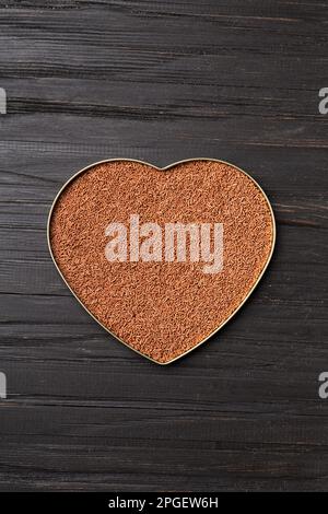 Chocolate chips are poured into a heart-shaped box on a wooden background with space for text. Milk chocolate in the shape of a heart on a dark Stock Photo