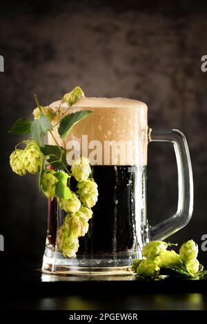 dark beer in a mug and green hop on wooden table on brown background. Oktoberfest. Beer Festival. Stock Photo