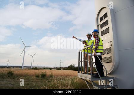 Two engineers in uniform with safety helmet pointing and using tablet for routine inspection. Stock Photo