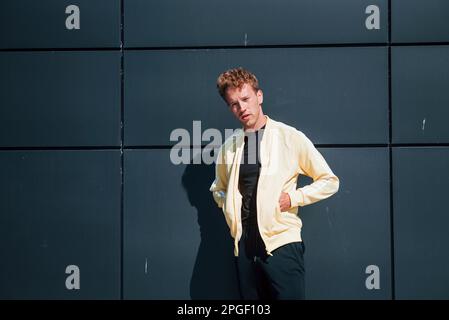 Fashionable young man in yellow shirt posing outdoors near building with black wall Stock Photo