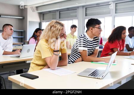 Bored student attending in class with a laptop at high school classroom. Group of students of a university.  Stock Photo