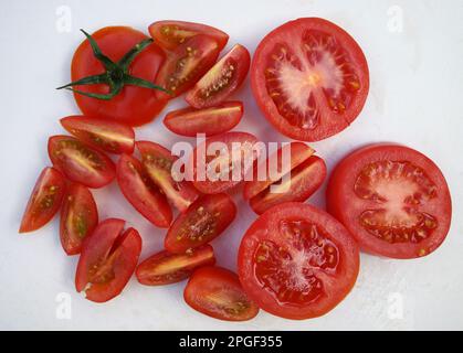 Sliced ​​red tomato combined with quartered cherry tomatoes on a white cutting board Stock Photo