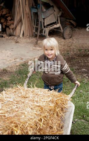 Portrait of a little boy pushing wheelbarrow in the farm, Bavaria, Germany Stock Photo