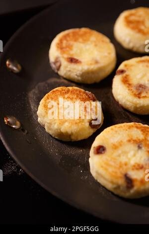 Delicious Ukrainian syrniki being cooked in a kitchen. Sweet cheese cakes frying on hot pan. Traditinal dessert food from Ukraine Stock Photo