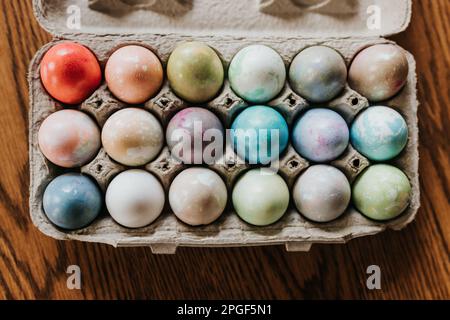 Overhead shot of dyed Easter eggs in carton sitting on kitchen table Stock Photo