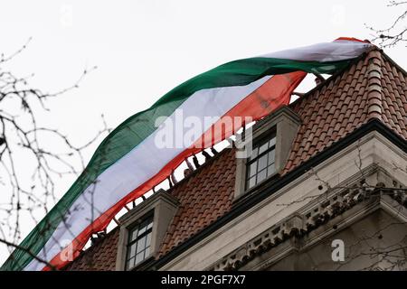 London, UK. 22 March, 2023. Staff members on the roof of the India High Commission wave a giant flag while watching Sikhs in the street below protest Stock Photo