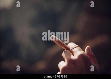 Boy smoking a marijuana joint on top of a mountain during sunset Stock Photo