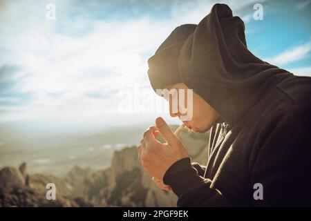 Boy smoking a marijuana joint on top of a mountain during sunset Stock Photo